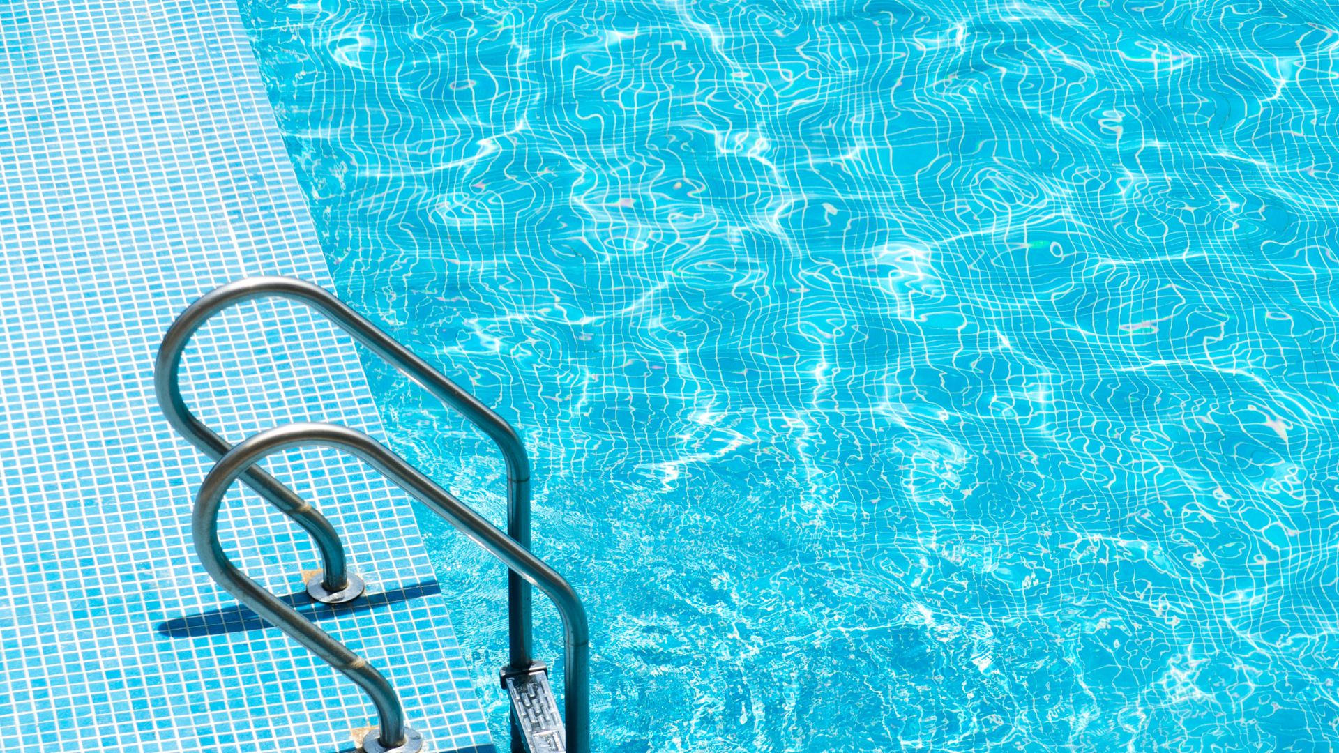 Swimming pool with clear blue water and metal handrail ladder