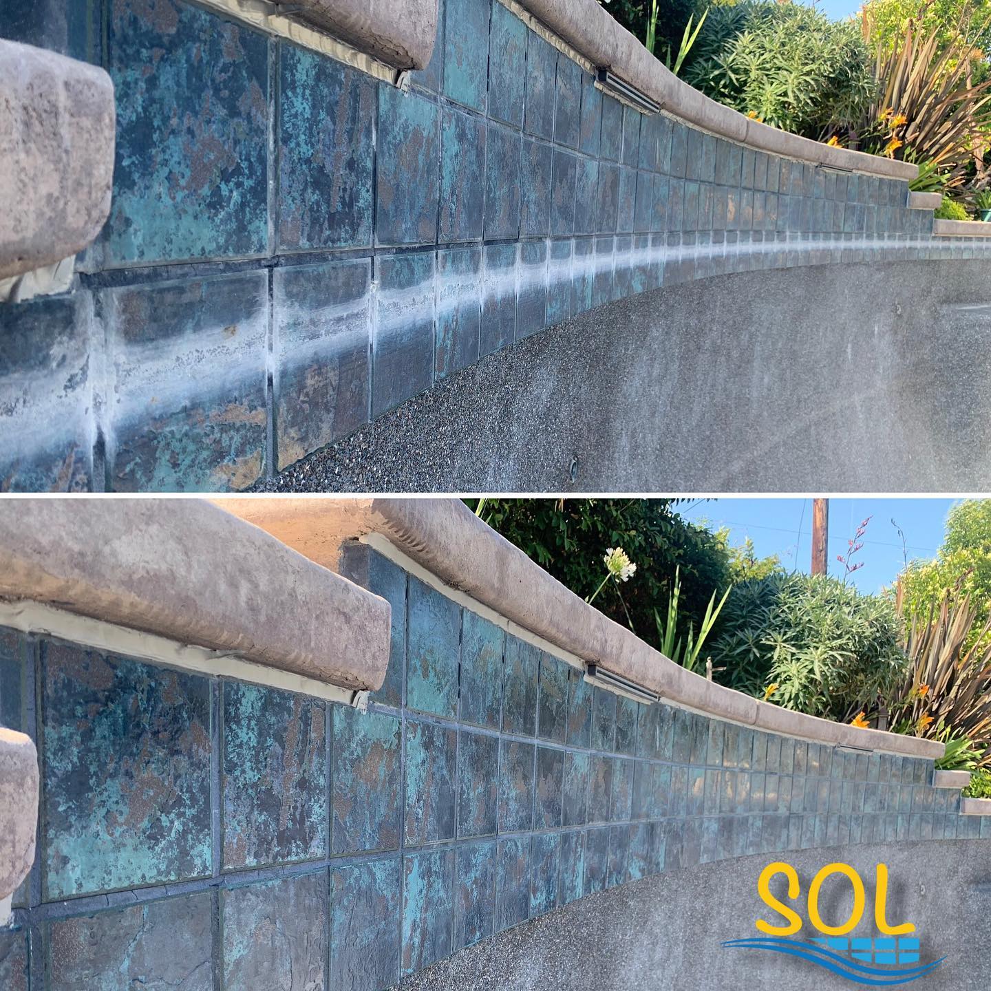 Curved blue-tiled wall with concrete base and plants in background