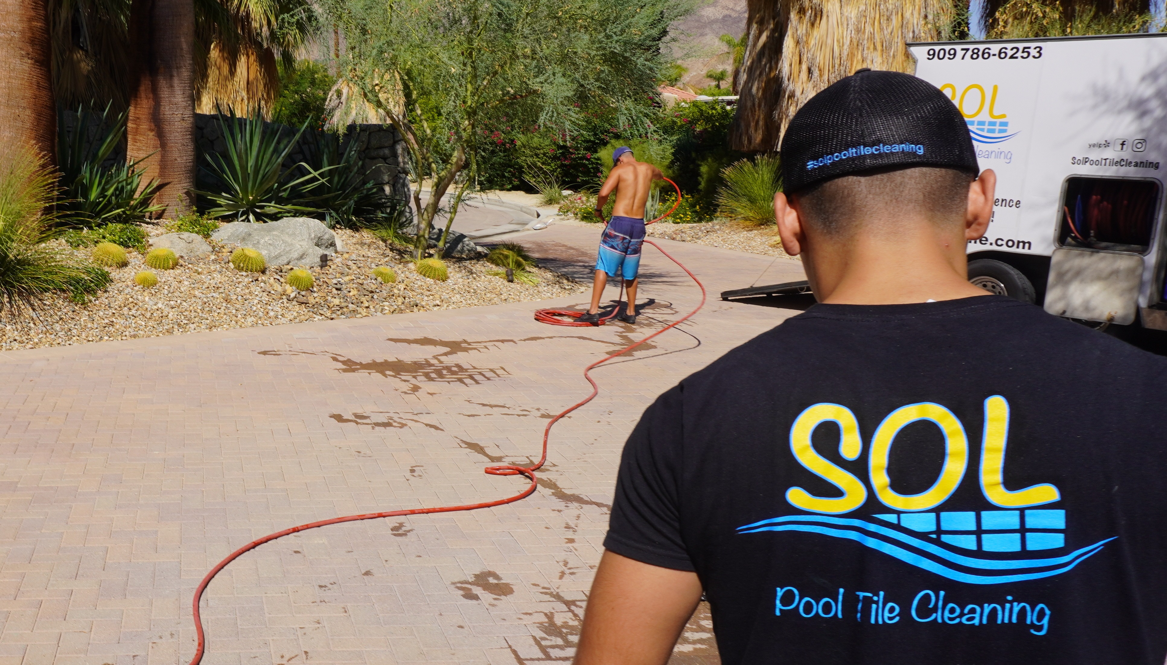 Pool tile cleaning worker using hose on landscaped outdoor patio
